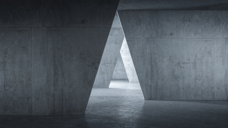 Abstract concrete architecture with triangular openings and stark lighting, creating a geometric, minimalistic interior space.
