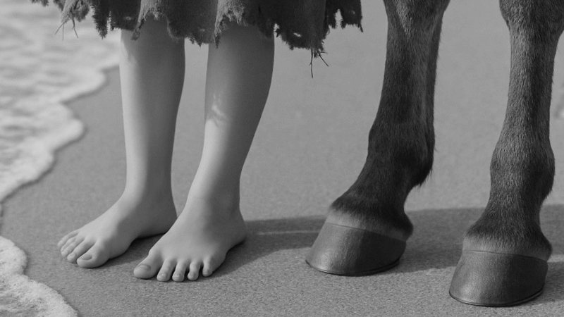 Child's feet and horse hooves on sandy beach near ocean waves, black and white photo.
